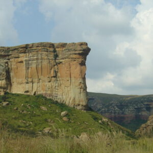 The sheer ochre sandstone face of the Brandwag Buttress rising above green grassy slopes, with further sandstone cliffs behind