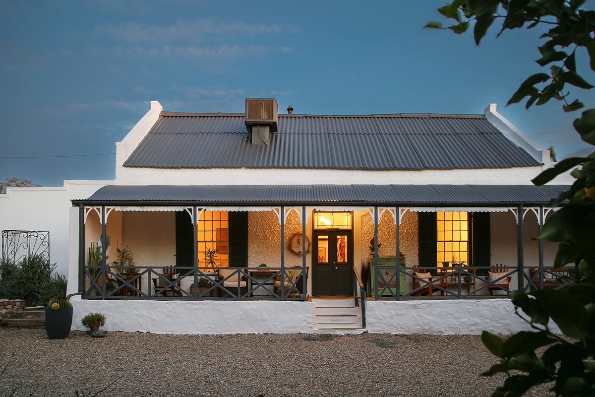 Veranda illuminata da lampade e facciata con frontone della fattoria al Dennehof Karoo Guesthouse