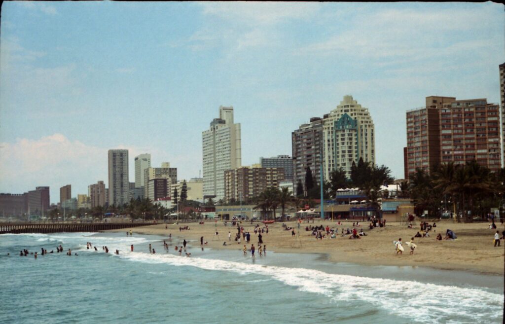 Surf breaking on a wide sandy beach with bathers and sunbathers, backed by palms and the high-rise beachfront skyline