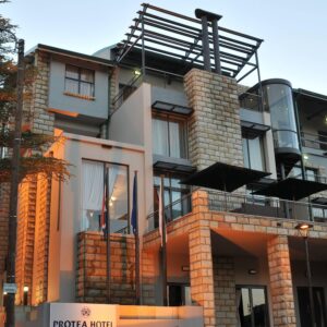 Sandstone and glass exterior of Protea Hotel Clarens at dusk with signage and balconies