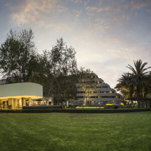 The Maslow hotel exterior at dusk across its lawn, with the lit garden restaurant pavilion