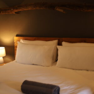 Quarto de lodge com roupa de cama branca, cabeceira de madeira e um ramo de madeira flutuada montado acima
